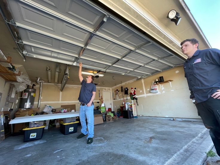 Two men examining a garage door installation in a cluttered garage.