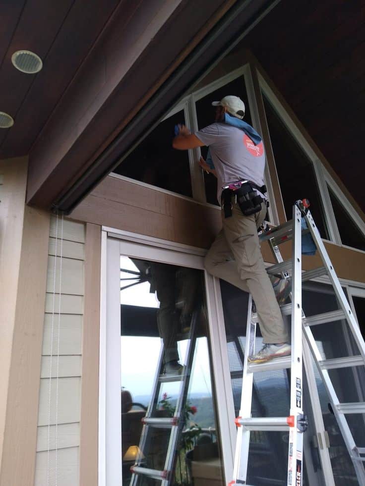 Man on ladder cleaning large window of modern house.