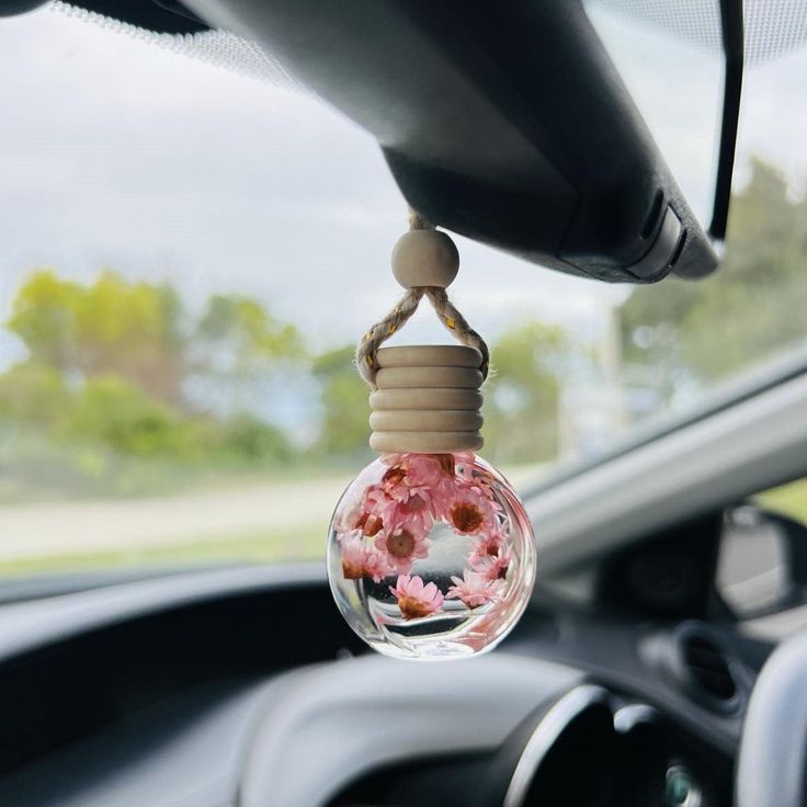 Hanging car air freshener with pink flowers inside, providing a refreshing scent and decorative touch to the interior.