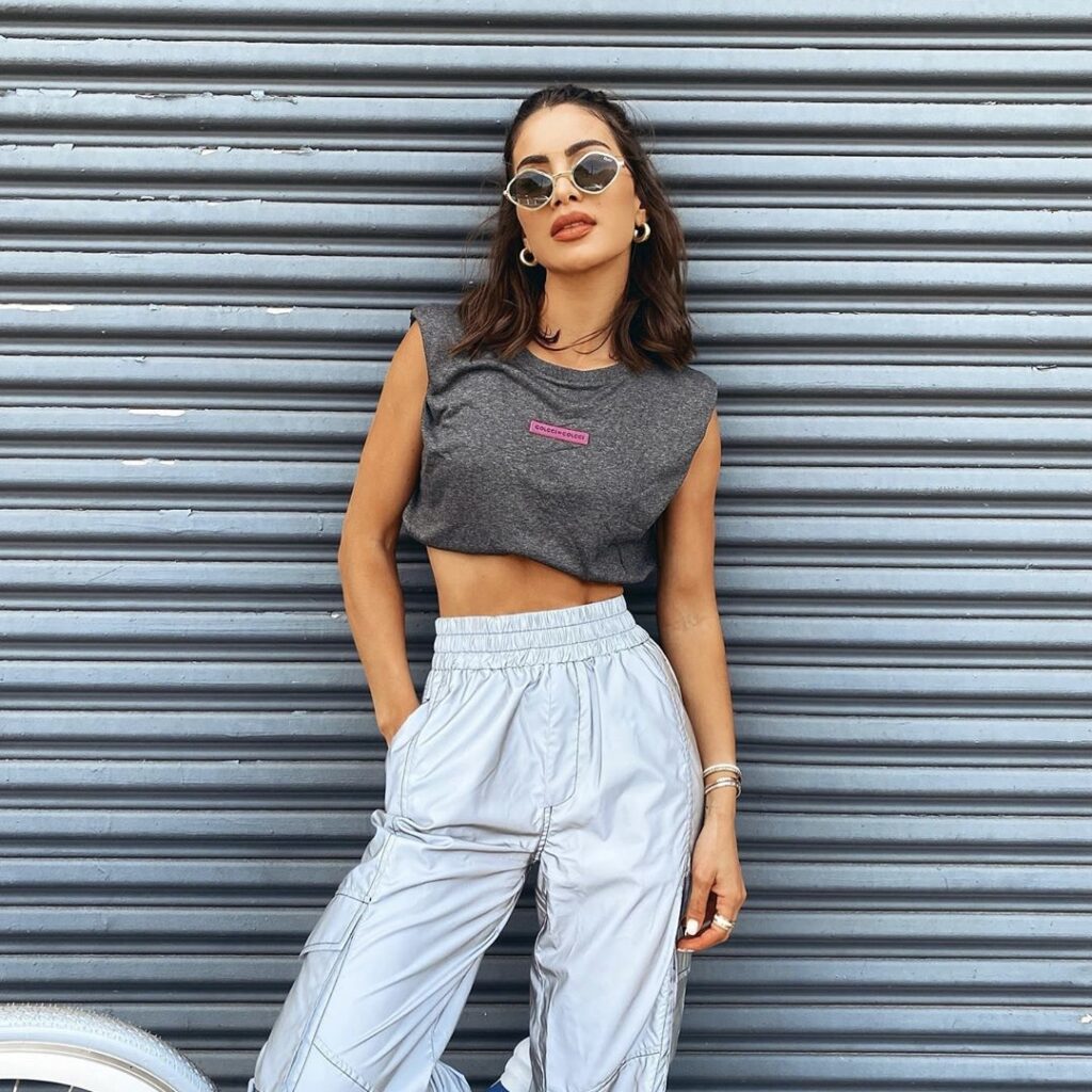Stylish woman in sunglasses and casual outfit posing against a corrugated metal background, exuding urban chic.