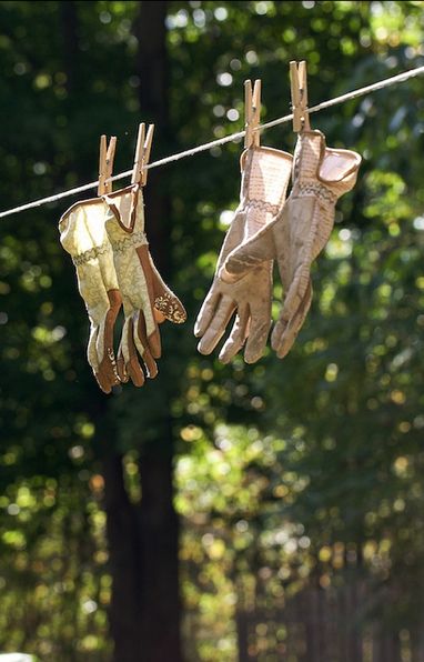 Work gloves hanging on a clothesline with clothespins in a sunny forest setting.