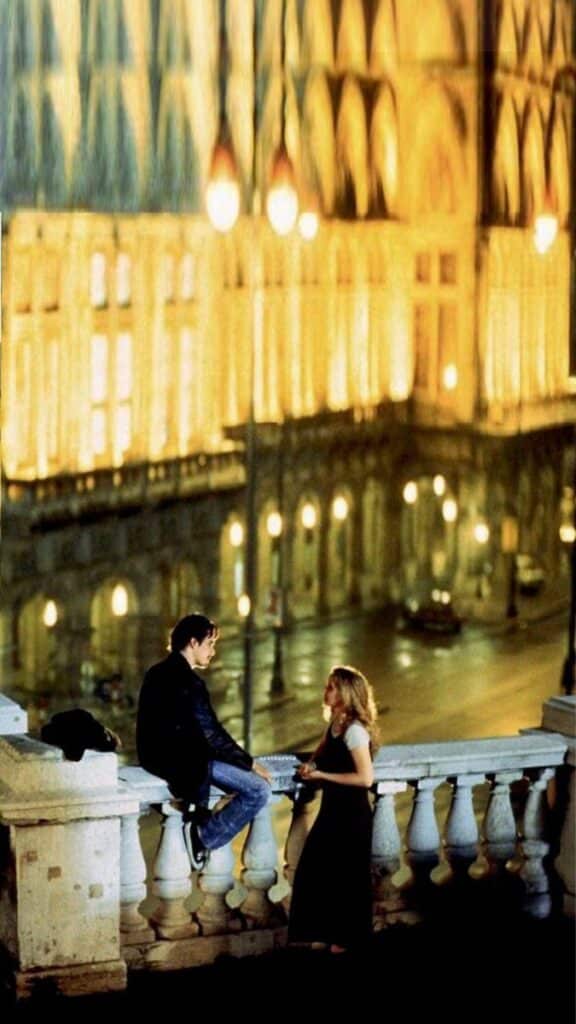 ced556cb424088bc787f9b388aac9d35 A couple converses on a ledge at night, with a beautifully lit building in the background. | Sky Rye Design A couple converses on a ledge at night, with a beautifully lit building in the background.