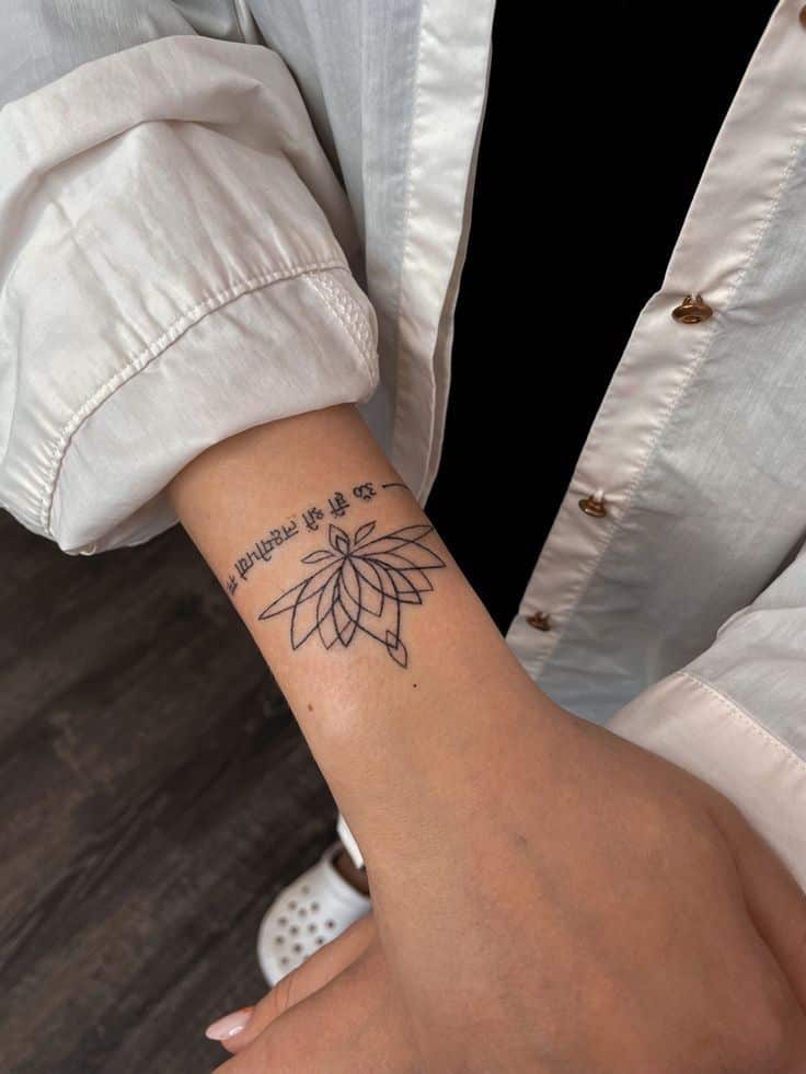 Minimalist geometric flower tattoo on wrist, paired with text, worn by person in white shirt.