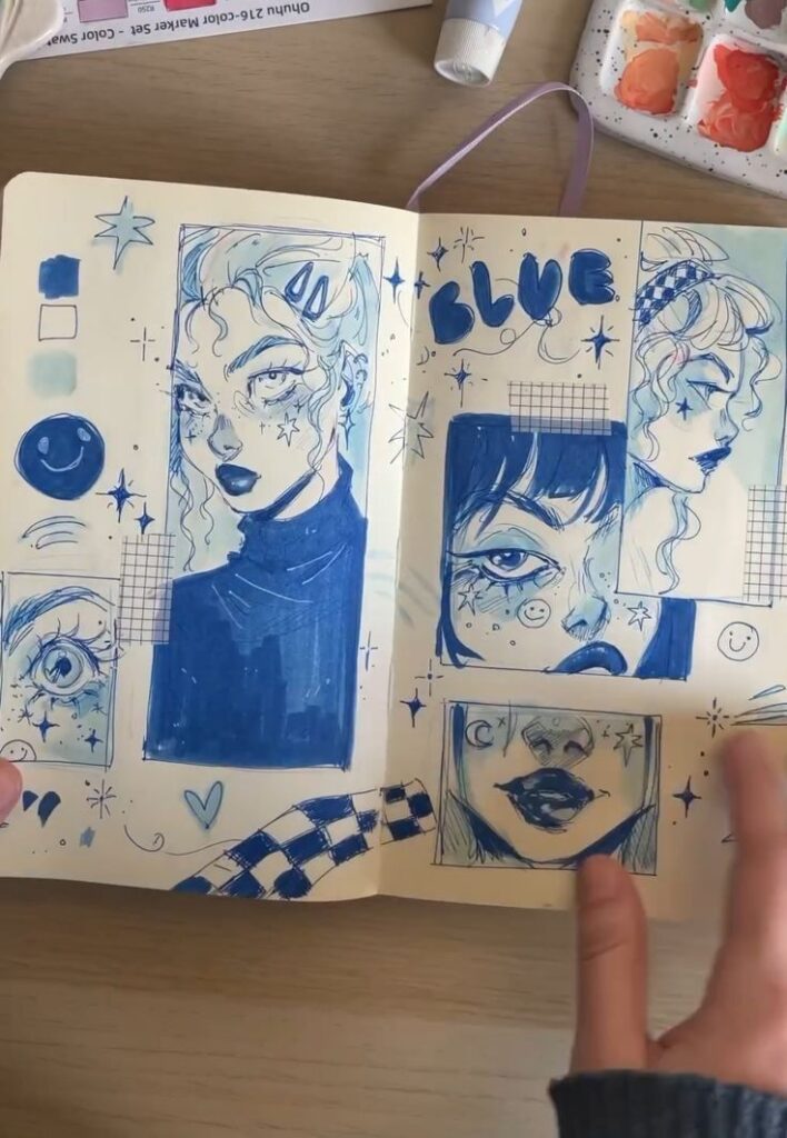 Blue-themed sketchbook art with various expressive faces, stars, and abstract designs on open pages.