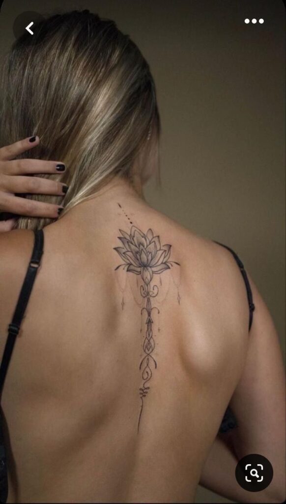 Woman with intricate lotus tattoo design on her back, highlighting detailed linework and elegant floral art.