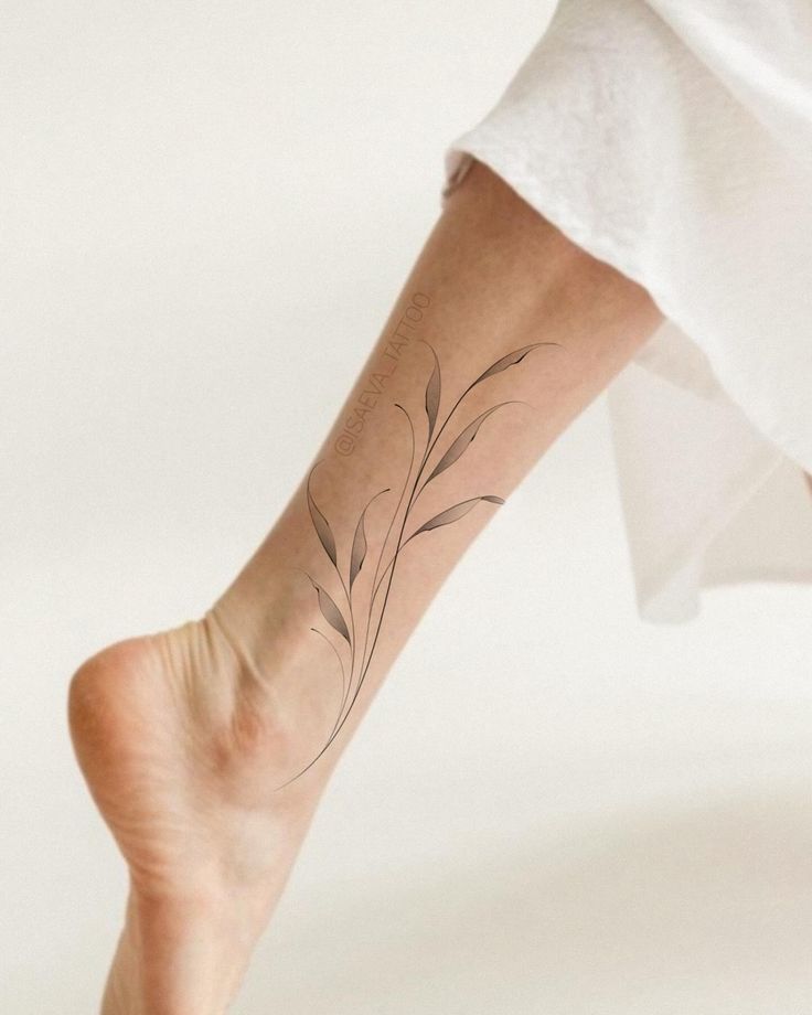 Minimalist leaf tattoo on calf, delicate design on leg, white background, showcasing elegant body art.