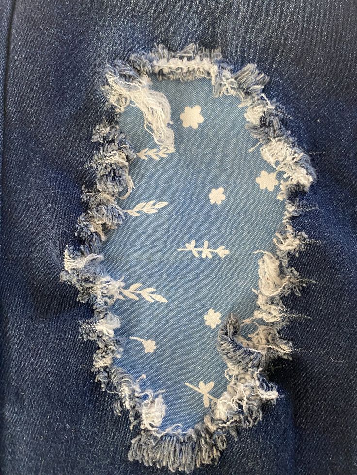 Frayed denim with floral patch detail, showcasing blue fabric with white flowers peeking through a torn jeans hole.
