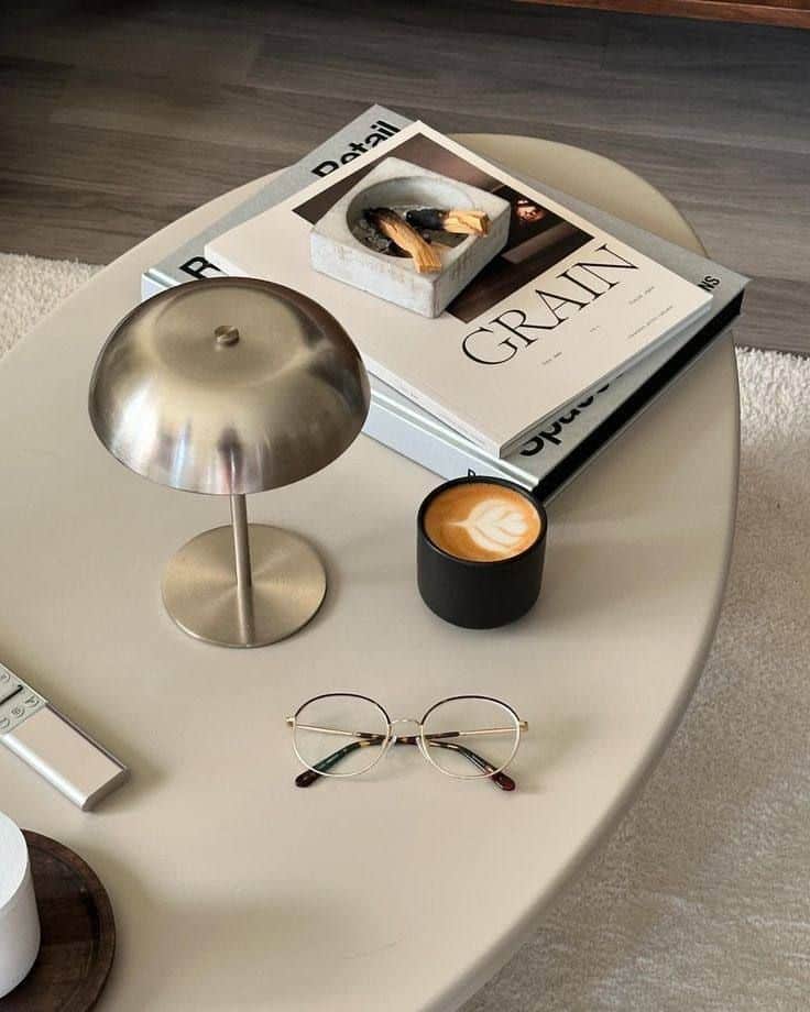 Modern coffee table with books, lamp, glasses, and cappuccino in a cozy setting.