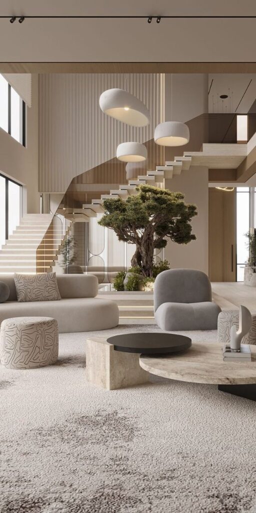 Modern living room with elegant staircase, large tree centerpiece, and stylish furniture in neutral tones.