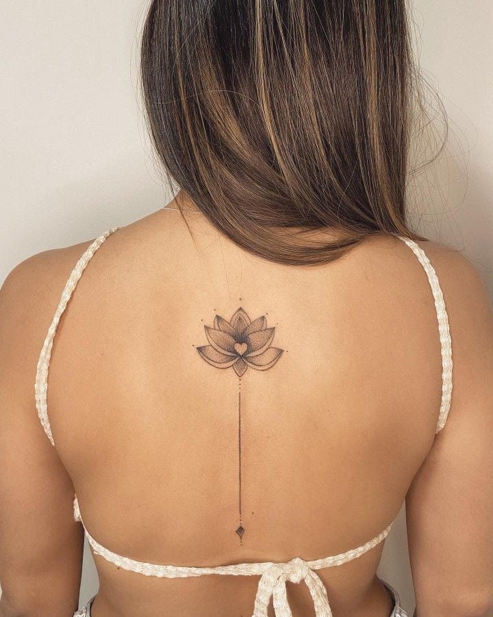 Back view of woman with intricate lotus tattoo, wearing a knotted white top, showcasing body art and style.