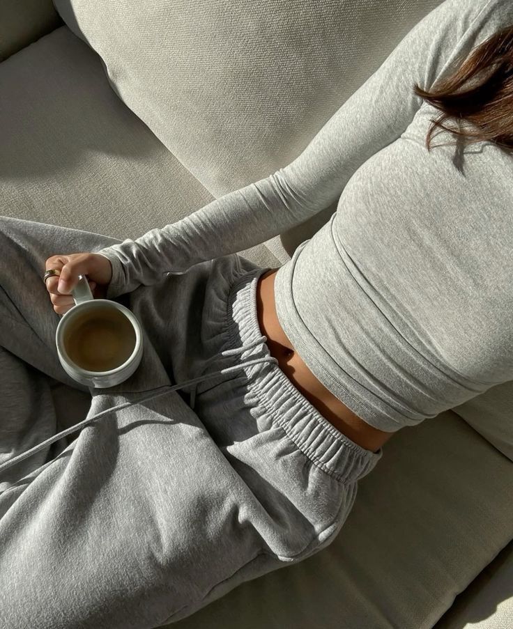 eaf9d5a7-d641-4fd8-b125-584081c908bc A person relaxes on a couch in grey loungewear, holding a mug, enjoying a cozy moment in natural light. | Sky Rye Design A person relaxes on a couch in grey loungewear, holding a mug, enjoying a cozy moment in natural light.