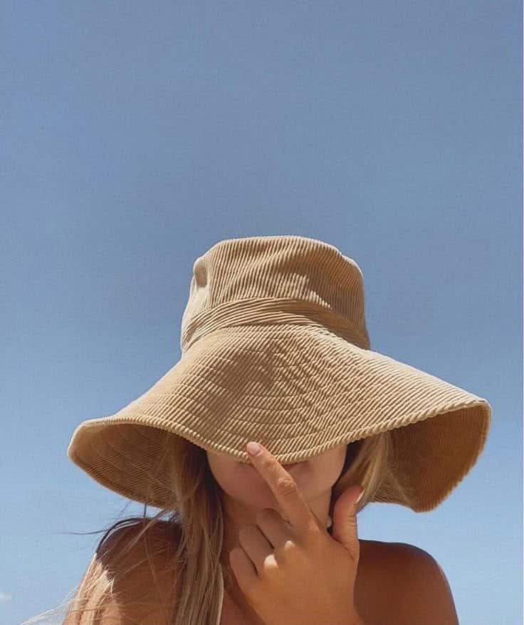 Woman wearing wide-brimmed hat against clear blue sky, partially covering face with hand, creating a serene summer vibe.