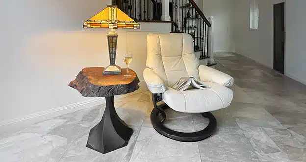 Cozy living room with a white recliner, a modern lamp on a wood table, and a glass of wine, perfect for relaxation.