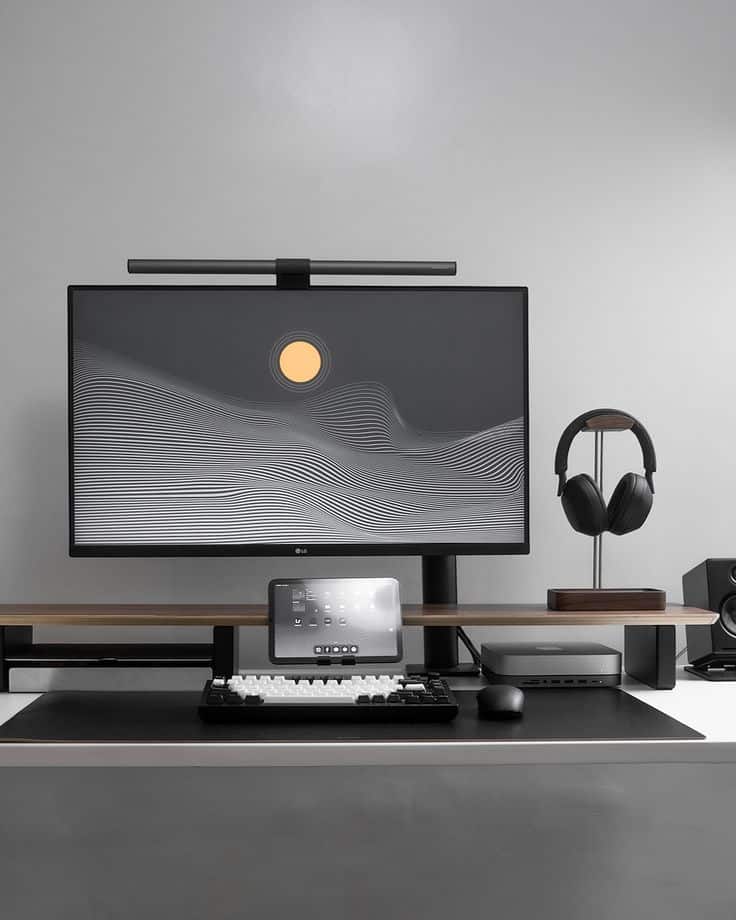 Minimalist computer desk setup with monitor, keyboard, headphones, and tablet, displaying a sleek monochrome design.