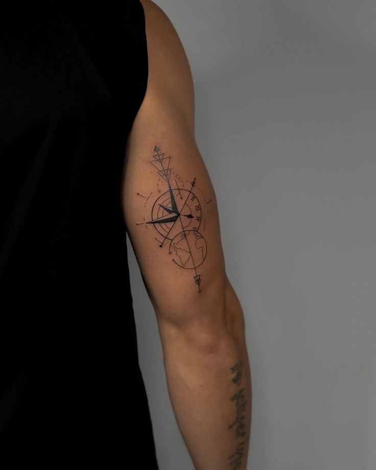 Geometric compass tattoo on upper arm, featuring earth and arrows, minimalist design in black ink.