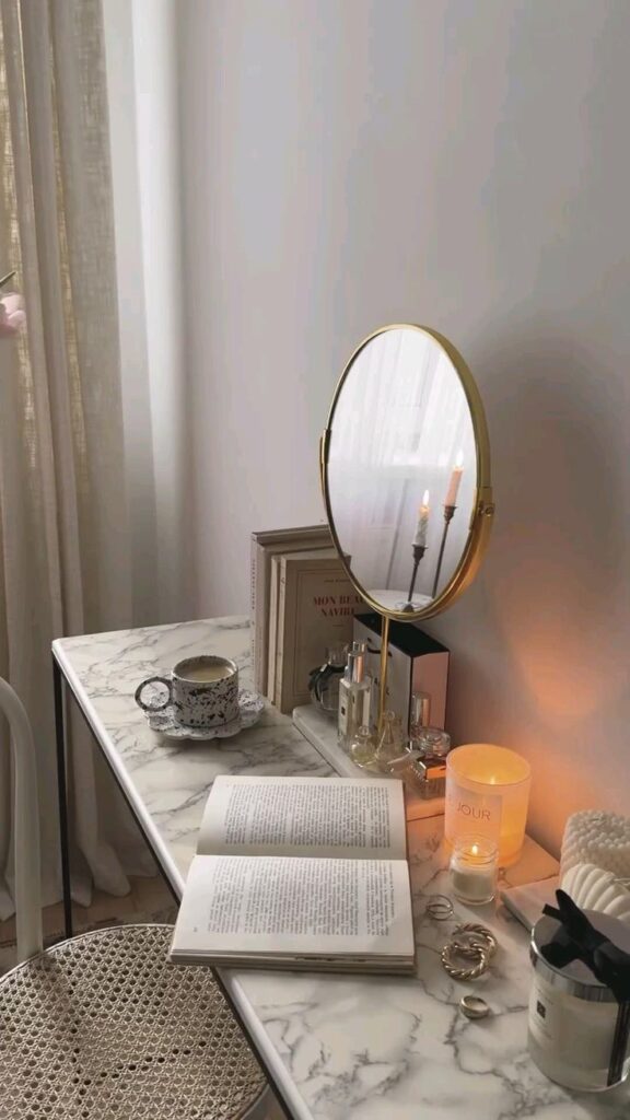 Cozy vanity setup with a round mirror, open book, coffee cup, and candles on a marble table, exuding calm and relaxation.