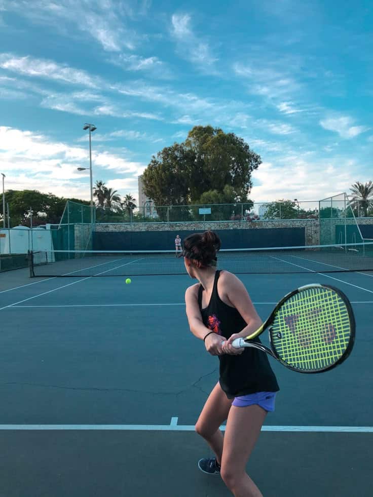 Person in sportswear playing tennis, preparing to hit a forehand on an outdoor court under a clear blue sky.
