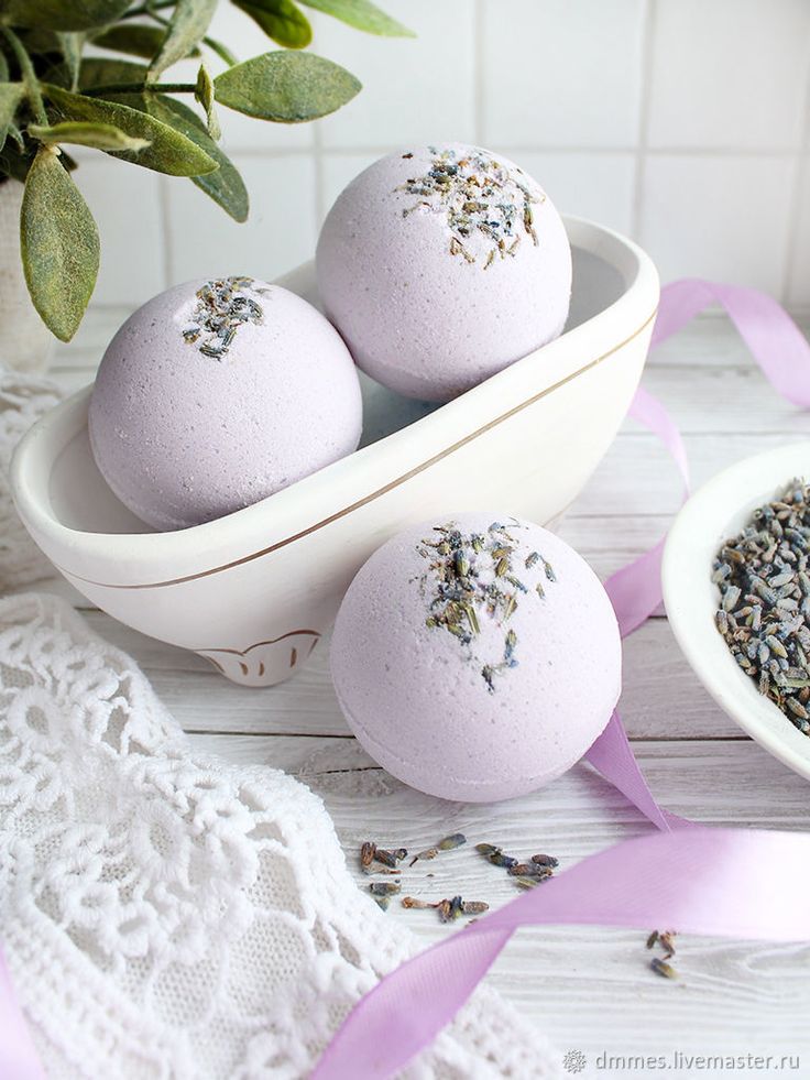 Lavender-scented bath bombs displayed in a ceramic bowl with decorative flowers and lace fabric.