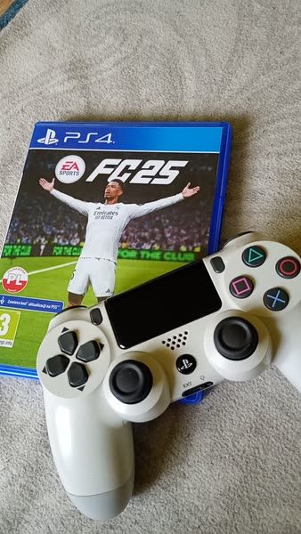 PS4 game FIFA 25 cover with player celebrating, alongside a white PlayStation controller on a soft surface.