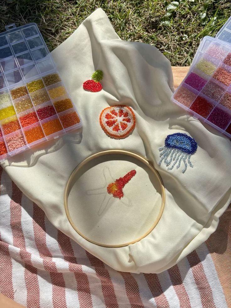 Embroidery project with colorful beads, showcasing fruit and jellyfish designs on fabric in sunny outdoor setting.