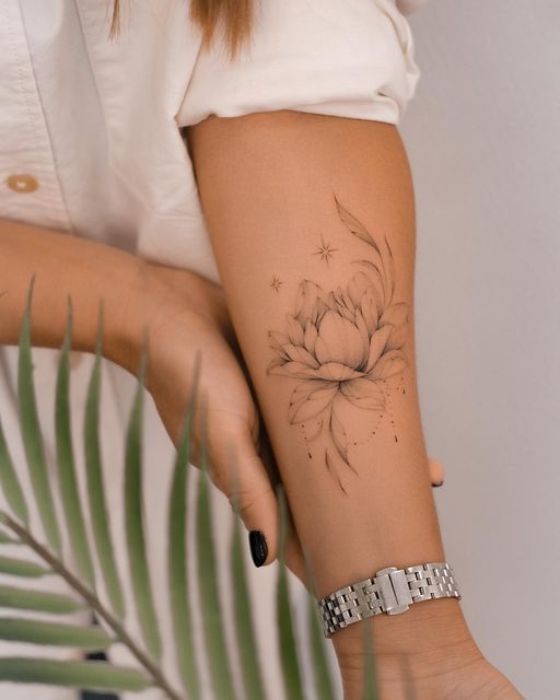 Forearm tattoo of a delicate flower design with stars, accented by a silver watch, next to a green leaf.