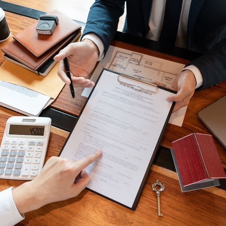 Business meeting with focus on purchase agreement document, calculator, pen, and office materials on a wooden desk.