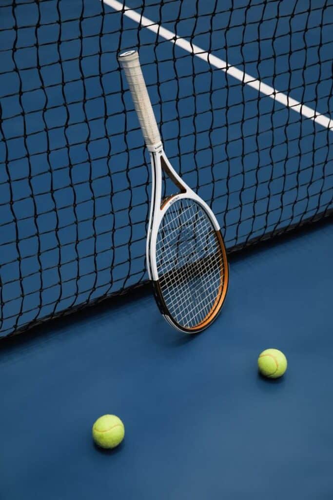 Tennis racket leaning on net with two tennis balls on a blue court background.