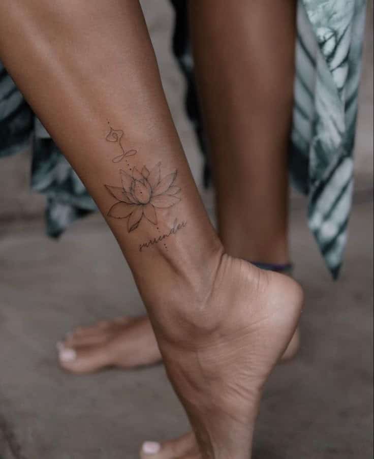 Lotus flower tattoo on ankle with word surrender, symbolizing peace and mindfulness.