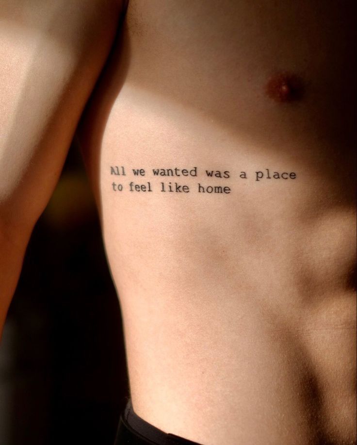 Side view of a torso with a typewriter-style tattoo reading All we wanted was a place to feel like home.