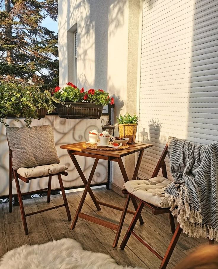 Cozy balcony with wooden furniture, green plants, and a table set for tea in the sunlight.