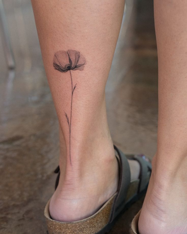 Minimalist poppy tattoo on calf, showcasing delicate lines and simplicity, paired with casual sandals.