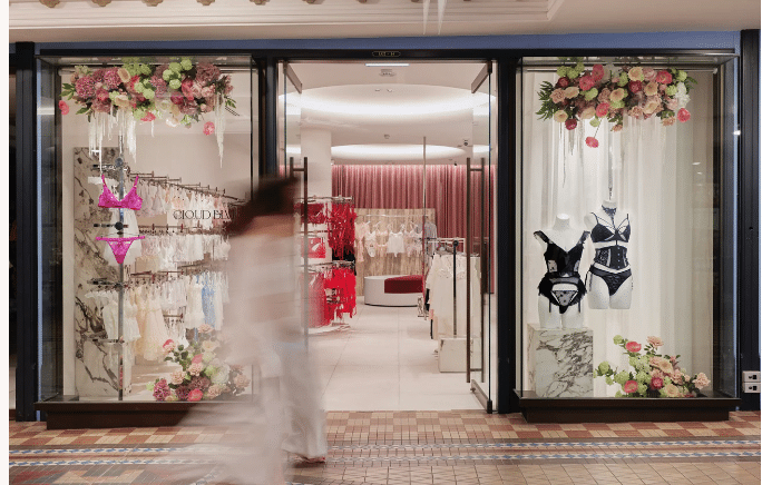 image1 Lingerie store display with elegant sets, floral decor, and a passerby in a mall setting. | Sky Rye Design Lingerie store display with elegant sets, floral decor, and a passerby in a mall setting.