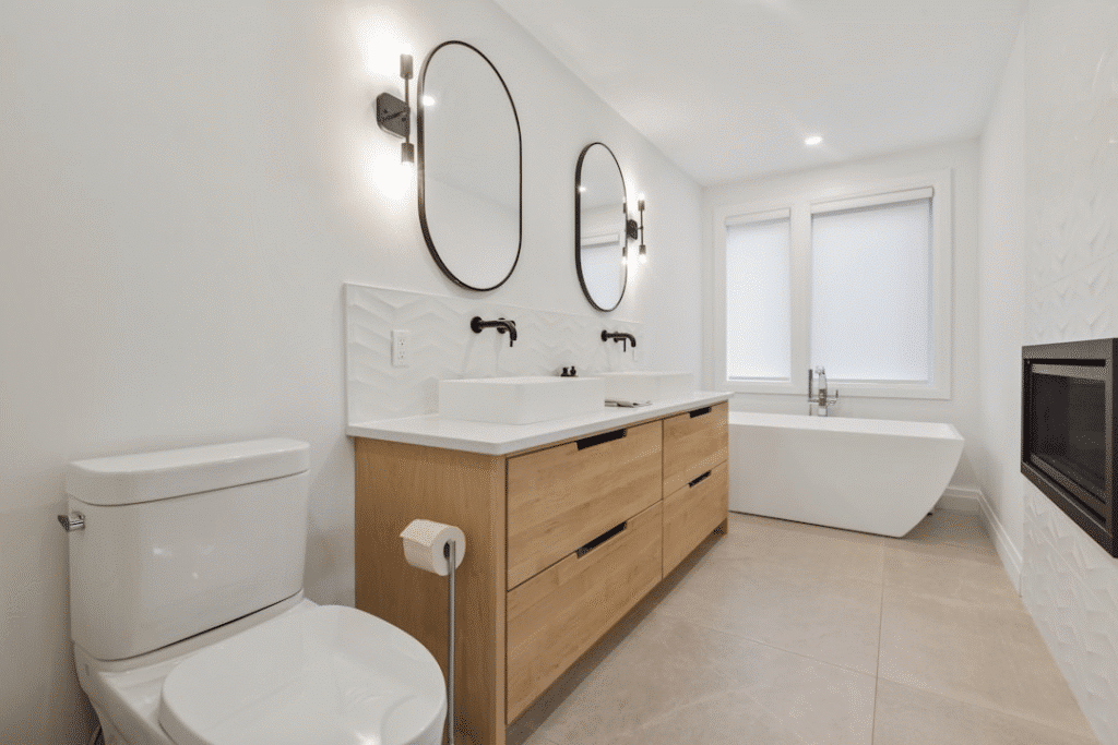 Modern bathroom with double vanity, mirrors, toilet, and freestanding tub. Elegant, minimalist design with neutral tones.