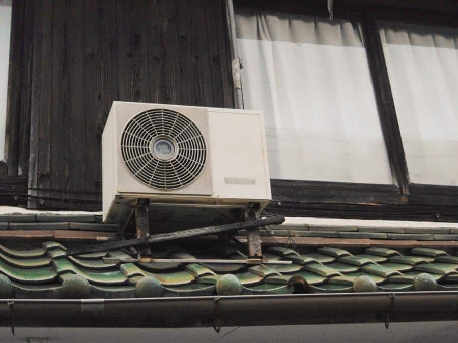 Outdoor air conditioning unit mounted on traditional green tile roof.
