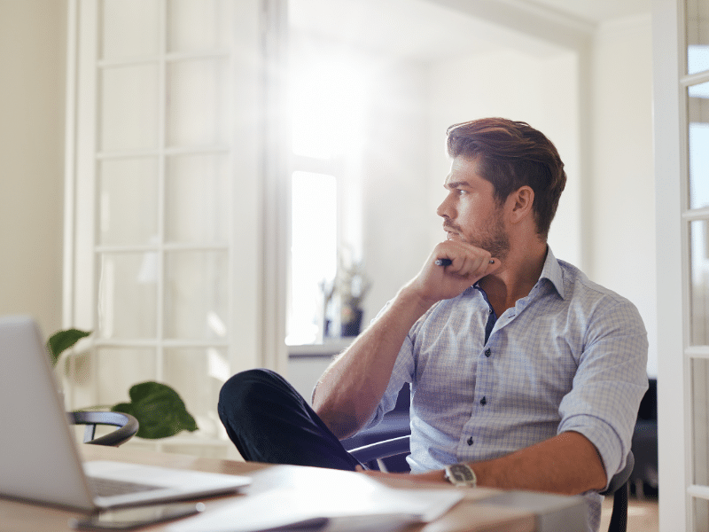 image2 Man in a shirt sitting at a desk, staring thoughtfully out a window, holding a pen, with a laptop in front. | Sky Rye Design Man in a shirt sitting at a desk, staring thoughtfully out a window, holding a pen, with a laptop in front.