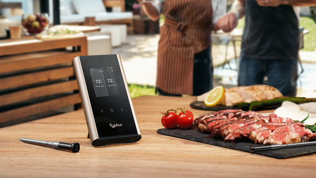 image3 Smart meat thermometer on table with grilled steak and vegetables in background. Perfect for precise cooking. | Sky Rye Design Smart meat thermometer on table with grilled steak and vegetables in background. Perfect for precise cooking.