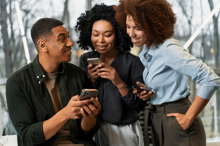 Group of people smiling and looking at smartphones indoors, engaging in conversation and enjoying technology.