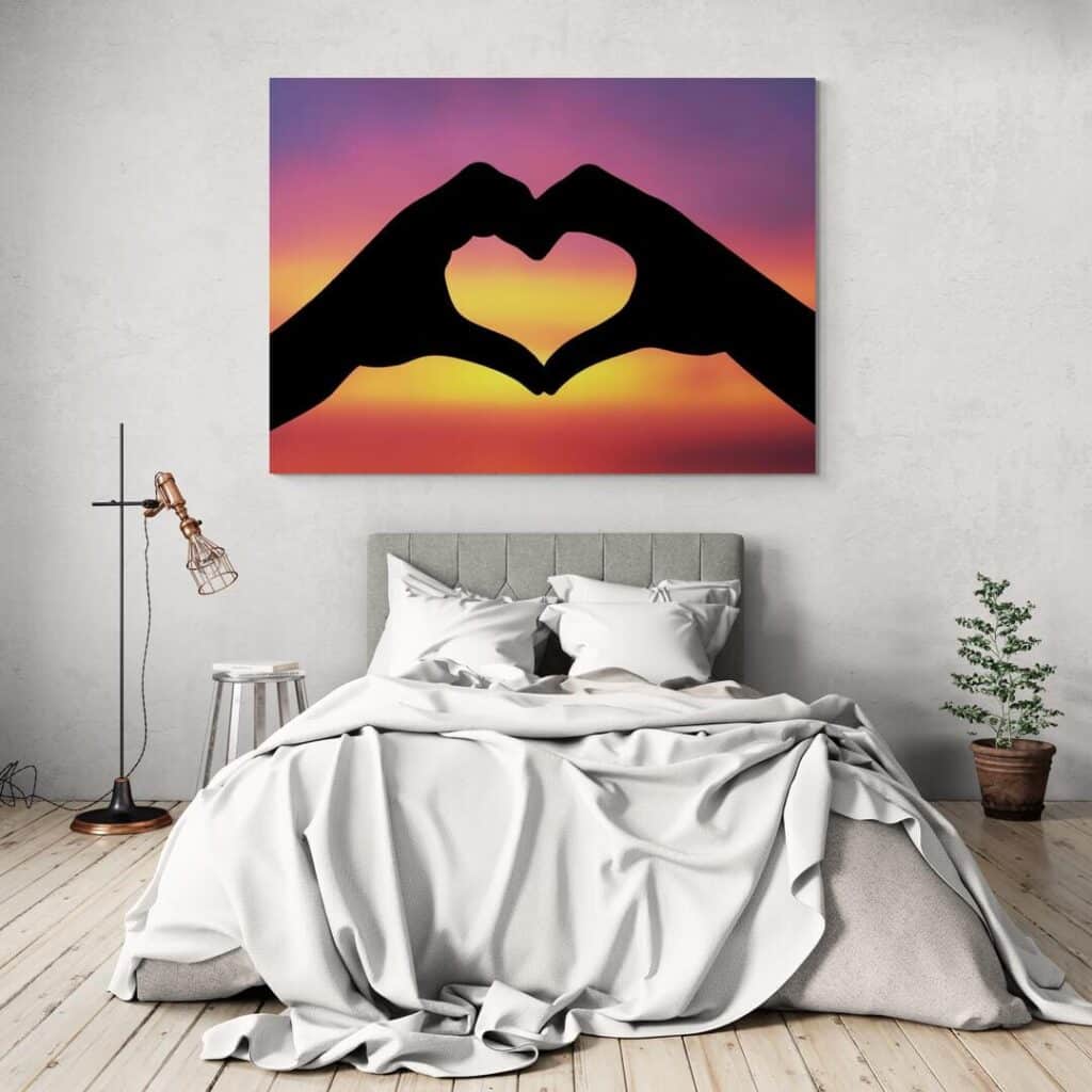 Cozy bedroom with heart hand silhouette art and colorful sunset canvas above bed.