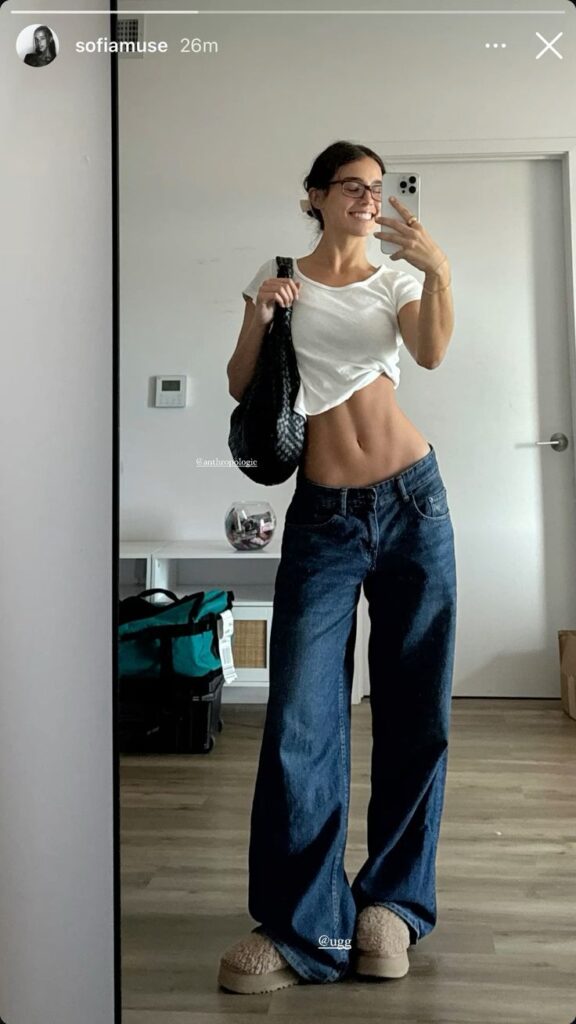 Smiling woman in casual wear taking a mirror selfie in a modern room.