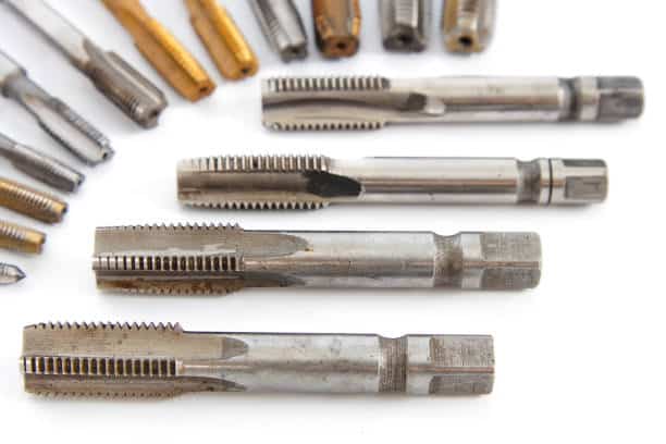 Close-up of various metal screw taps arranged on a white background for threading and machining.