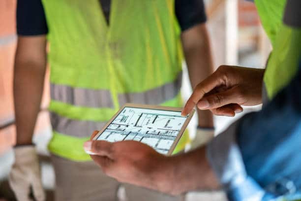 Construction workers reviewing building plans on a tablet onsite.