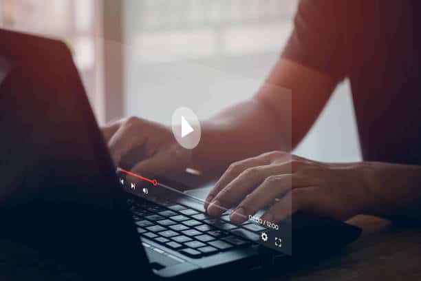 Person typing on a laptop with a video paused on the screen, showcasing media playback controls.