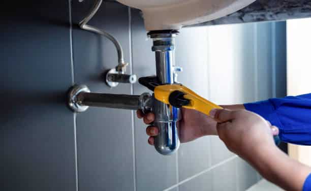 Plumber using wrench to fix a leaking pipe under a sink, highlighting professional plumbing repair services.
