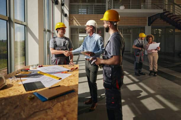 Construction team discussing project plans in a building, with workers shaking hands and reviewing blueprints.