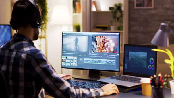 Video editor working on dual monitors, wearing headphones, in a home office with modern decor and ambient lighting.