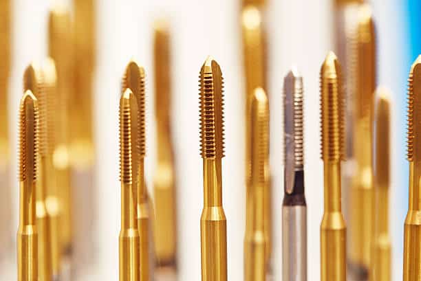 Gold and silver machine taps for threading, arranged vertically, with a blurred background.