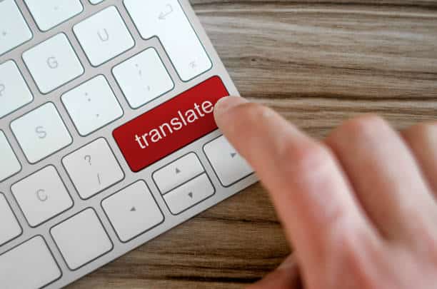 Finger pressing red translate button on keyboard, symbolizing language translation and digital communication.