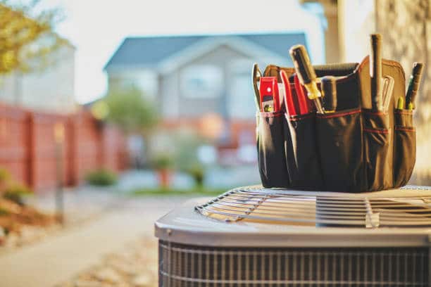 Tool bag on outdoor air conditioning unit with blurred house in background, representing home maintenance and repair.