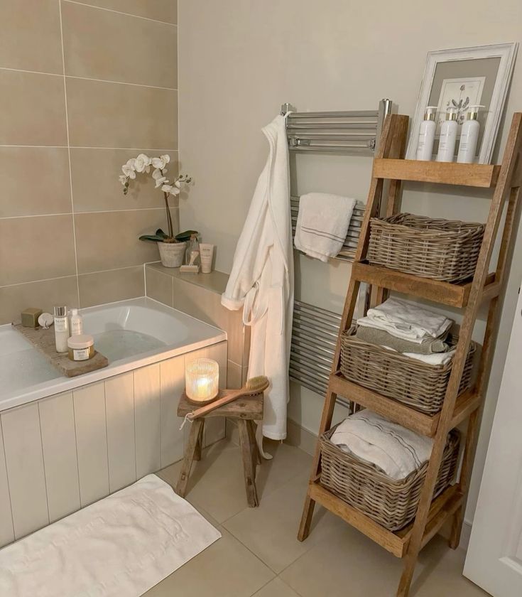 jesslifeandhome Cozy bathroom with candle-lit bath, white robe, towel ladder, and wicker storage baskets for a spa-like experience. | Sky Rye Design Cozy bathroom with candle-lit bath, white robe, towel ladder, and wicker storage baskets for a spa-like experience.