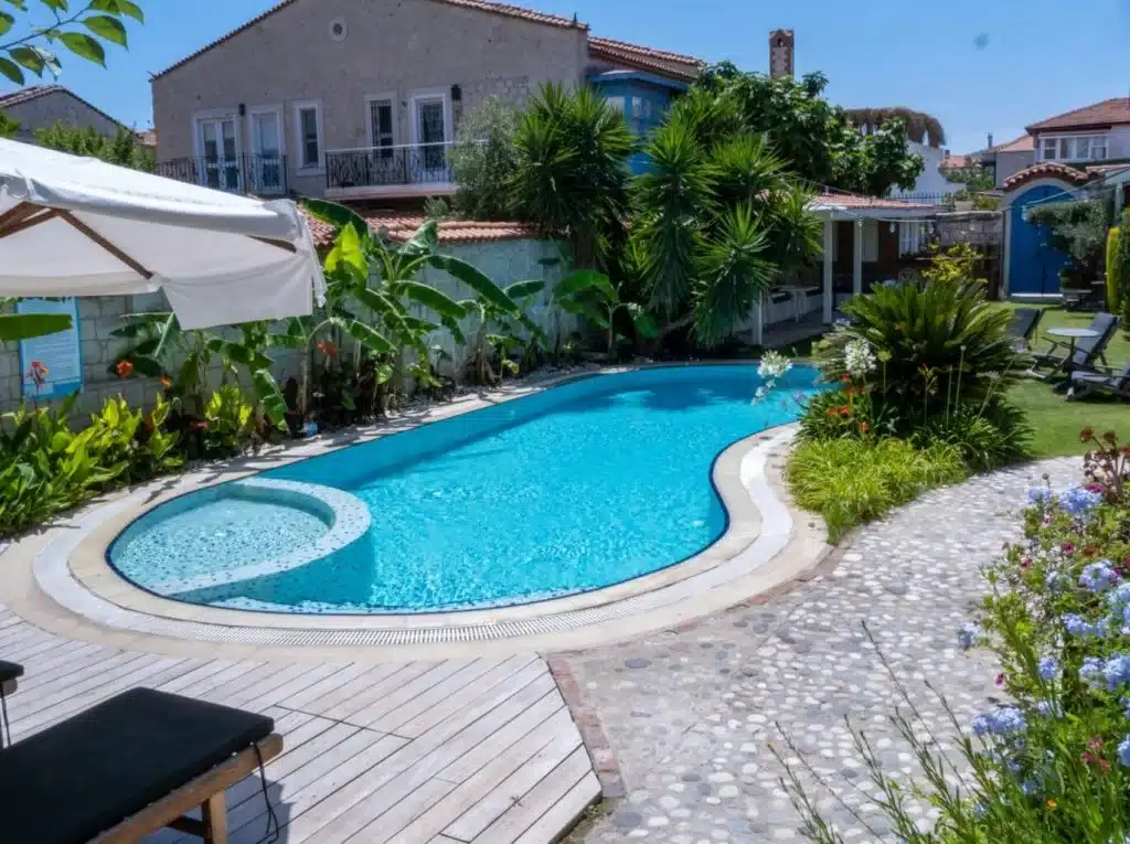Tropical garden with a curved pool and lounge chairs, surrounded by vibrant flowers and greenery under blue skies.